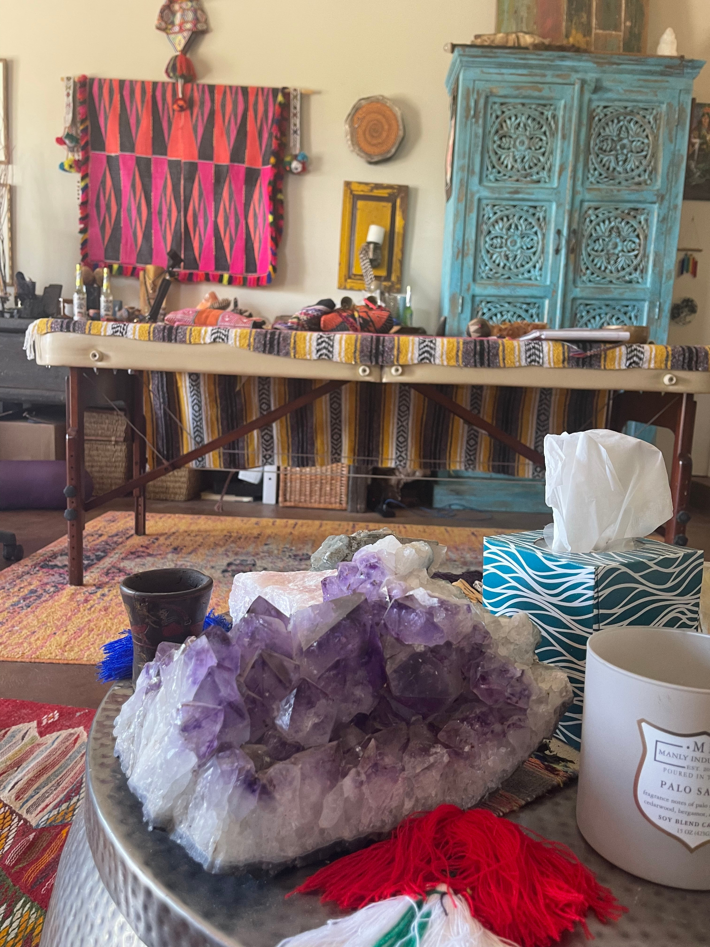 Living room with colorful artwork, crystal table, and woven rugs